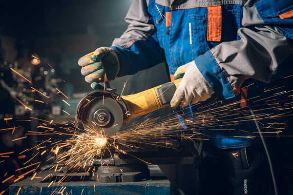 A worker in special clothes and goggles uses an angle grinder to grind metal, with sparks flying. (442229936)