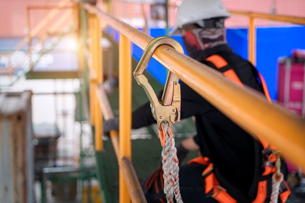 Construction worker wearing safety gear with a fall protection hook attached to a railing on a job site. (363521728)